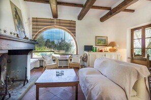Ein gemütliches Zimmer mit Kamin, einer Couch, einem Tisch und Blick durch ein großes, rundes Fenster.