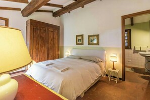 Ein Schlafzimmer mit Bett, Nachttischlampen, einem Holzschrank und einem durch eine offene Tür einsehbaren Badezimmer.