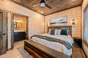 A bedroom with a wooden ceiling, a bed with multiple pillows, a bench, a nightstand, and a painting on the wall. - Luxe Cabin · Rooftop Bar · Indoor Pool · Mtn View (Pigeon Forge)