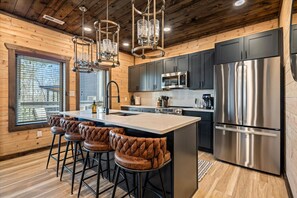 A modern kitchen with a central island, bar stools, stainless steel appliances, and wooden paneling. - LUXE-Mtn Views-1 mi to PKWY-Pool-Rooftop Bar-Pets (Pigeon Forge)