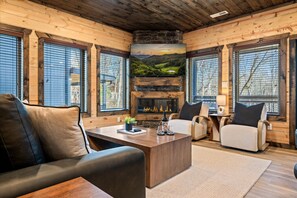 A cozy log cabin interior with a fireplace, leather seating, and large windows. - LUXE-Mtn Views-1 mi to PKWY-Pool-Rooftop Bar-Pets (Pigeon Forge)