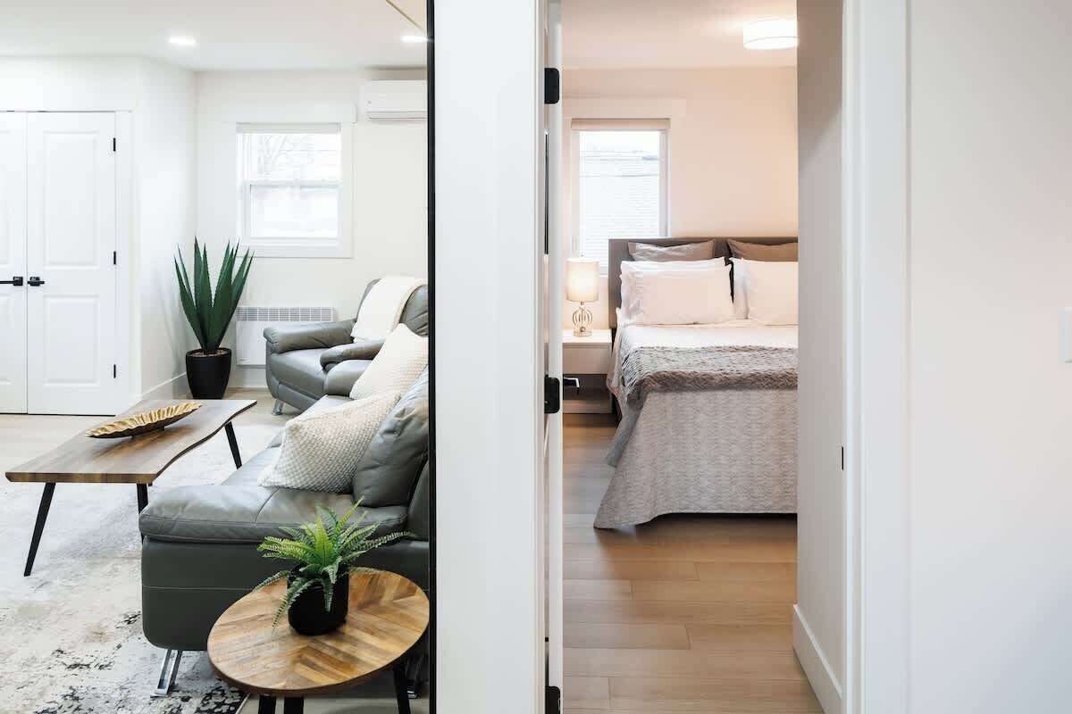 Una habitación moderna con sofá, una mesita, una planta en maceta y una cama con mesita de noche.