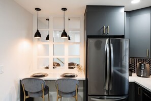 Une cuisine moderne dotée d’un réfrigérateur en acier inoxydable, de deux luminaires suspendus et d’un plan de travail blanc.