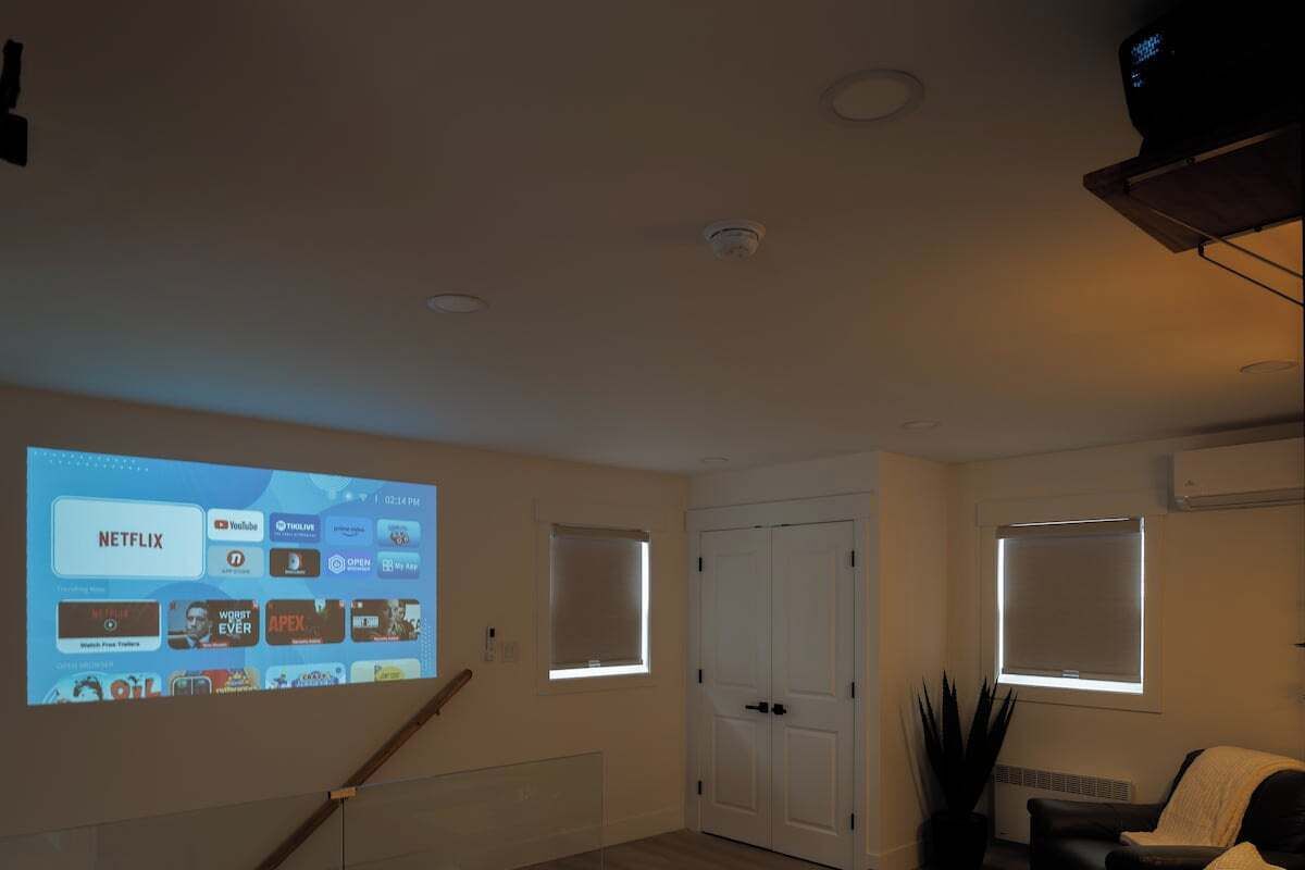 Ein Wohnzimmer mit einer Projektionsleinwand, die Streamingdienste zeigt, einer Tür und einem Fenster.
