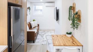 Een kleine keuken met een roestvrijstalen koelkast, een houten eettafel en een bank met kussens.