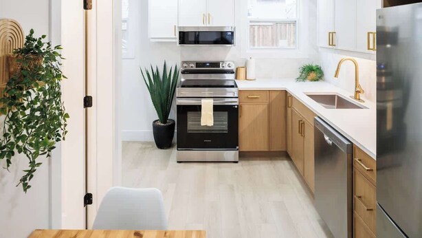 Een moderne keuken met witte kasten, roestvrijstalen apparatuur en een houten eettafel.