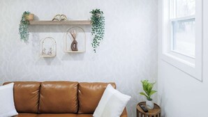 Een kamer met een bruine leren bank, een klein houten bijzettafeltje met een plant, een plank met decoratieve objecten en een raam.