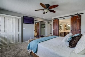 Ein Schlafzimmer mit Bett, Deckenventilator, Kleiderschrank und einem durchgegangene Tür erkennbaren Badezimmer.