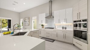 Una cucina moderna con mobili bianchi, elettrodomestici in acciaio inossidabile e un'isola centrale.