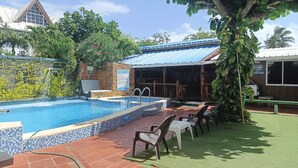 A swimming pool with tiled edges, a covered seating area, and a brick patio.