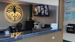 A hotel reception desk with a large illuminated logo, a flat-screen TV, and a welcome sign.