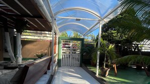 A covered walkway with a bench, potted plants, and a gate leading to a garden area.