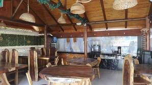 A rustic restaurant interior with wooden tables and chairs, hanging wicker lamps, and a marble countertop.