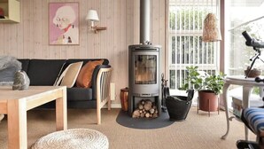 Een gezellige woonkamer met een houtkachel, een bank, een bijzettafeltje en potplanten.