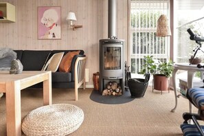 A cozy living room with a wood-burning stove, a sofa, a coffee table, and potted plants. - Summerhouse by the Little Belt with sea view (Haderslev)
