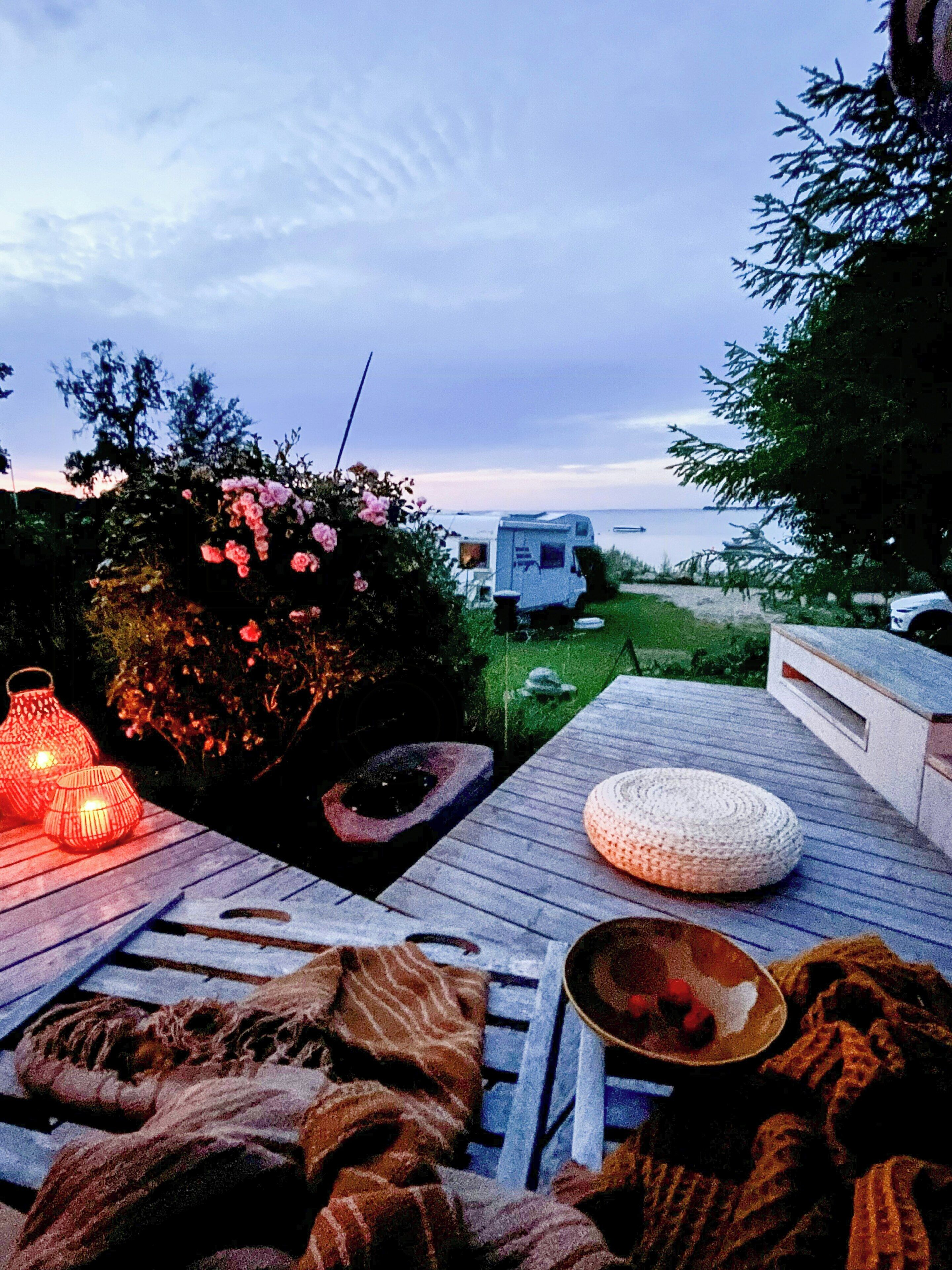 A deck with a blanket, a woven pouf, and a lantern.