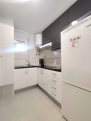 A kitchen with white cabinets, a black countertop, and a white refrigerator. - Pigem Apartment (Salou)