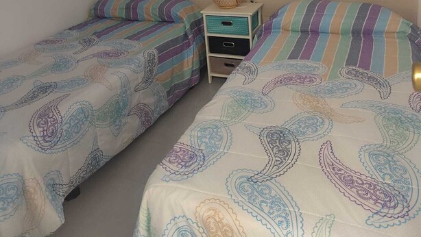 Een slaapkamer met twee eenpersoonsbedden, een nachtkastje met een lamp en een raam met jaloezieën.