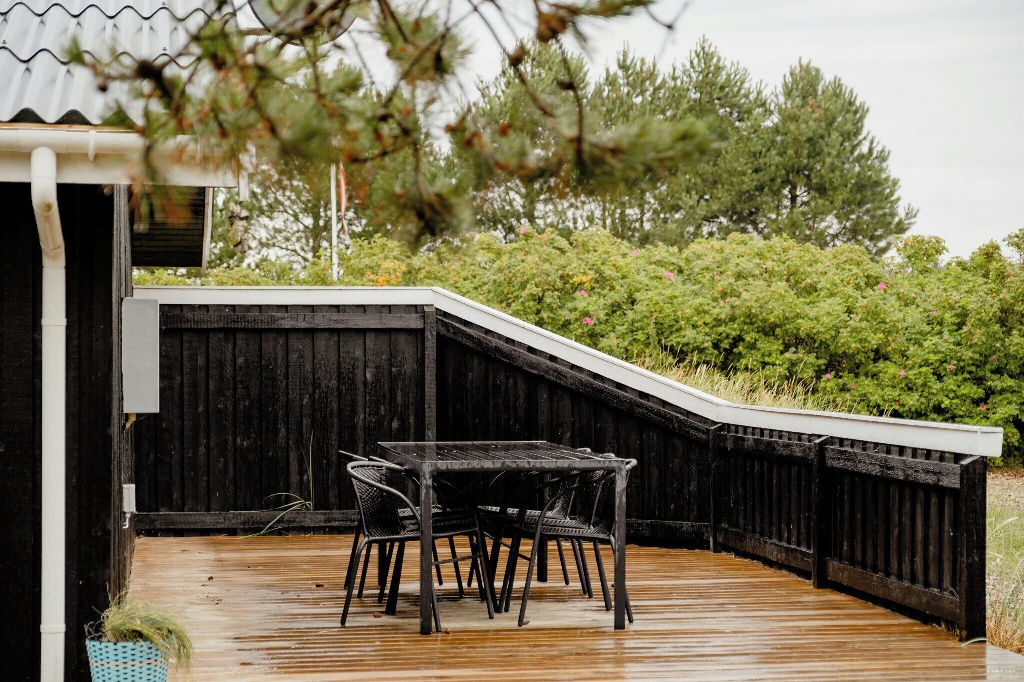 Eine Holzterrasse mit Tisch und Stühlen, umgeben von einem schwarzen Zaun und viel Grün.