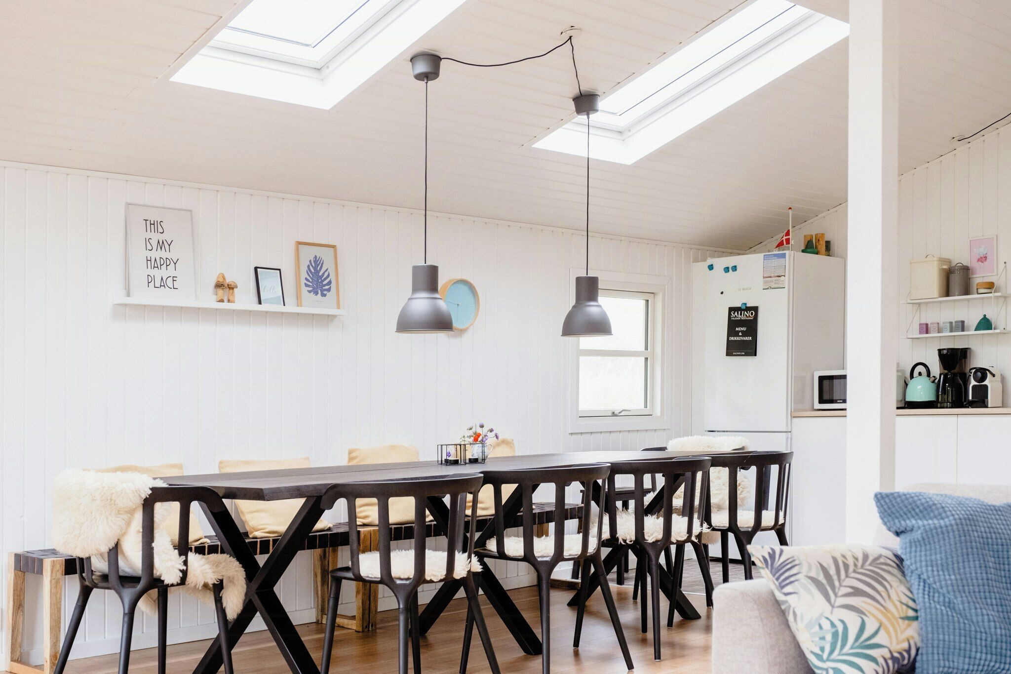 A modern kitchen with a dining area, featuring a skylight, pendant lights, and a refrigerator.