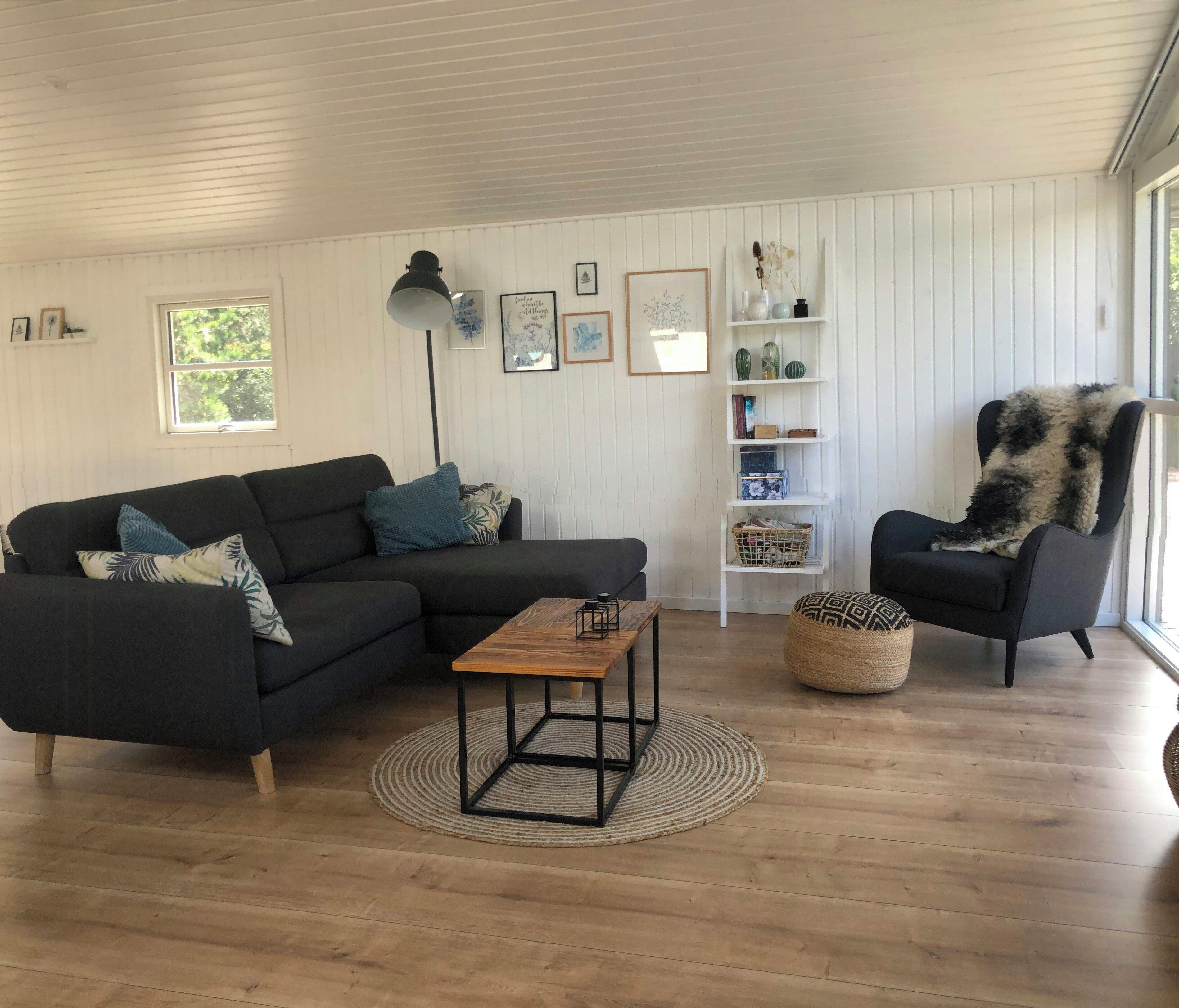 A living room with a sectional sofa, a coffee table, a side table, a chair, a floor lamp, a bookshelf, and a window.