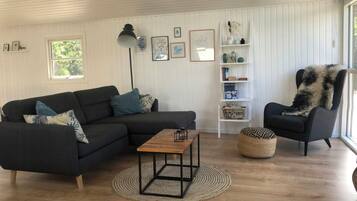 A living room with a sectional sofa, a coffee table, a side table, a chair, a floor lamp, a bookshelf, and a window.