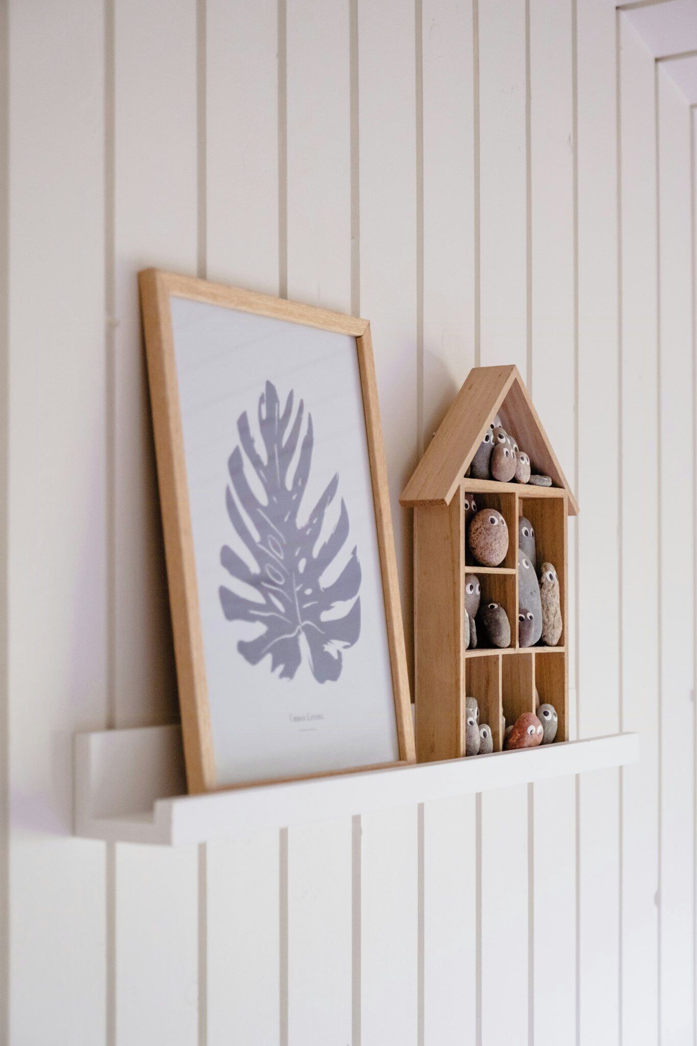 A framed leaf artwork and a wooden house-shaped shelf with rocks.