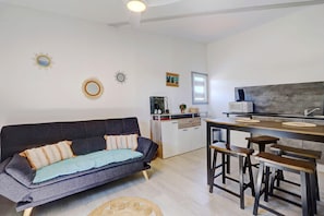 A modern living space with a sofa, kitchen area, and bar stools. - Liyann - Proche plage - Terre Sainte (Saint-Pierre)