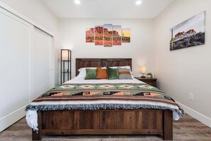 A bedroom with a wooden bed, a wall-mounted side table, a bedside lamp, and two wall art pieces. - Cozy Mega-Duplex | 8BR Summer Retreat (Tucson)