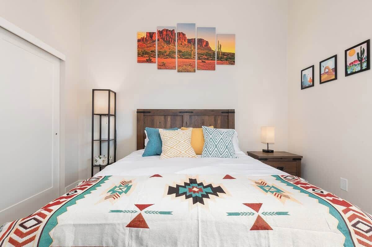 A bed with a patterned bedspread, a nightstand with a lamp, a wall-mounted artwork, and a framed picture on the wall.