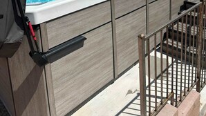 Una vasca idromassaggio con una persona sdraiata all'interno, circondata da un pontile in legno e una ringhiera metallica.