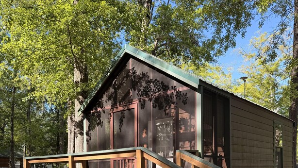 A small wooden cabin with a wooden deck and stairs leading to the entrance.