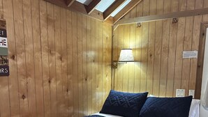 A wooden-paneled room with a bed, a wall-mounted lamp, and a skylight.