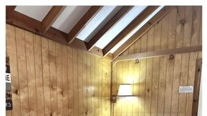 Una habitación de madera con una cama, una lámpara de pared y un techo inclinado.