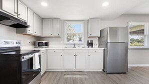 Una cocina moderna con armarios blancos, electrodomésticos de acero inoxidable y un ventanal con persianas.