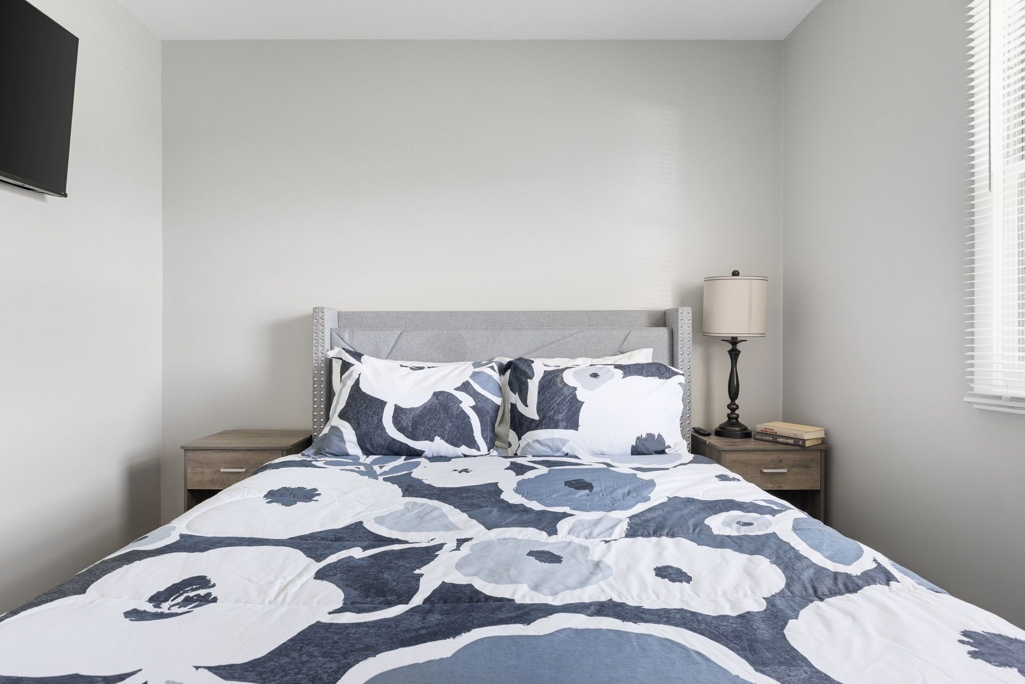 A bedroom with a bed, nightstands, a lamp, and a window with blinds.