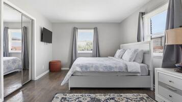 Ein Schlafzimmer mit Bett, Fernseher, Nachttisch, Teppich und einem Fenster mit Vorhängen.