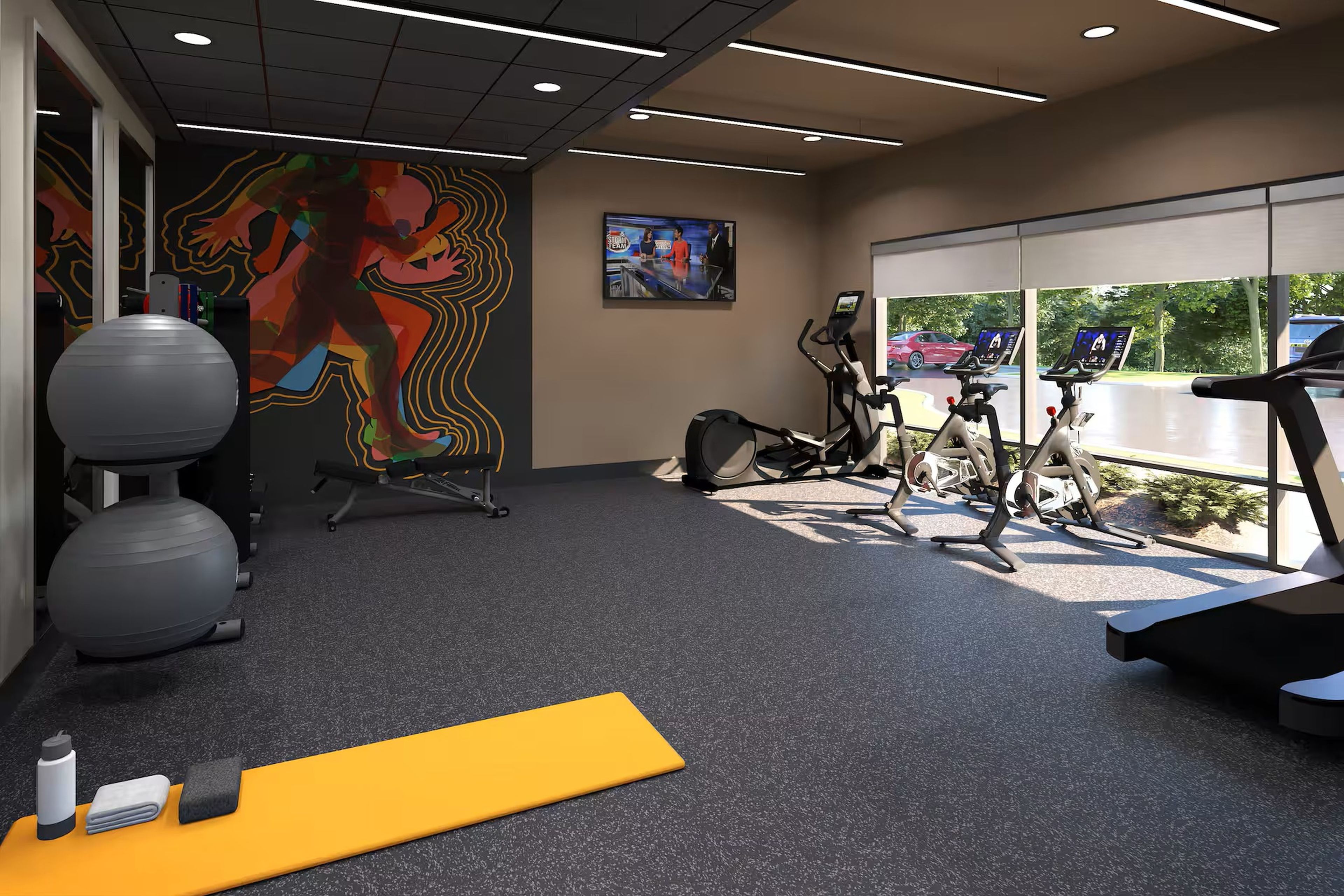Een sportschool met fitnessapparatuur, een groot raam en een kleurrijke muurschildering.