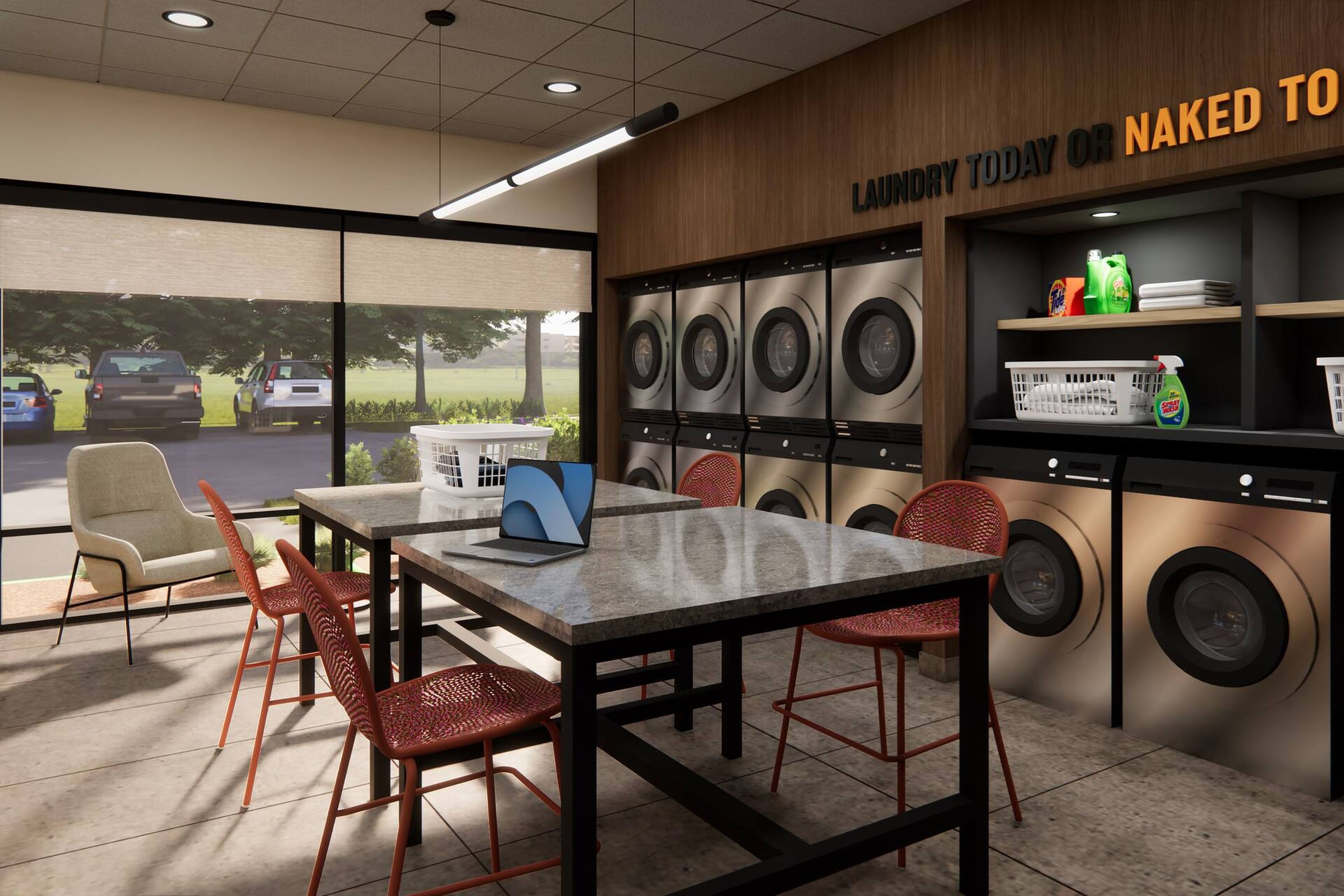 A laundromat with multiple washing machines, a table with chairs, and a view of the outside.