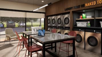 A laundromat with multiple washing machines, a table with chairs, and a view of the outside.
