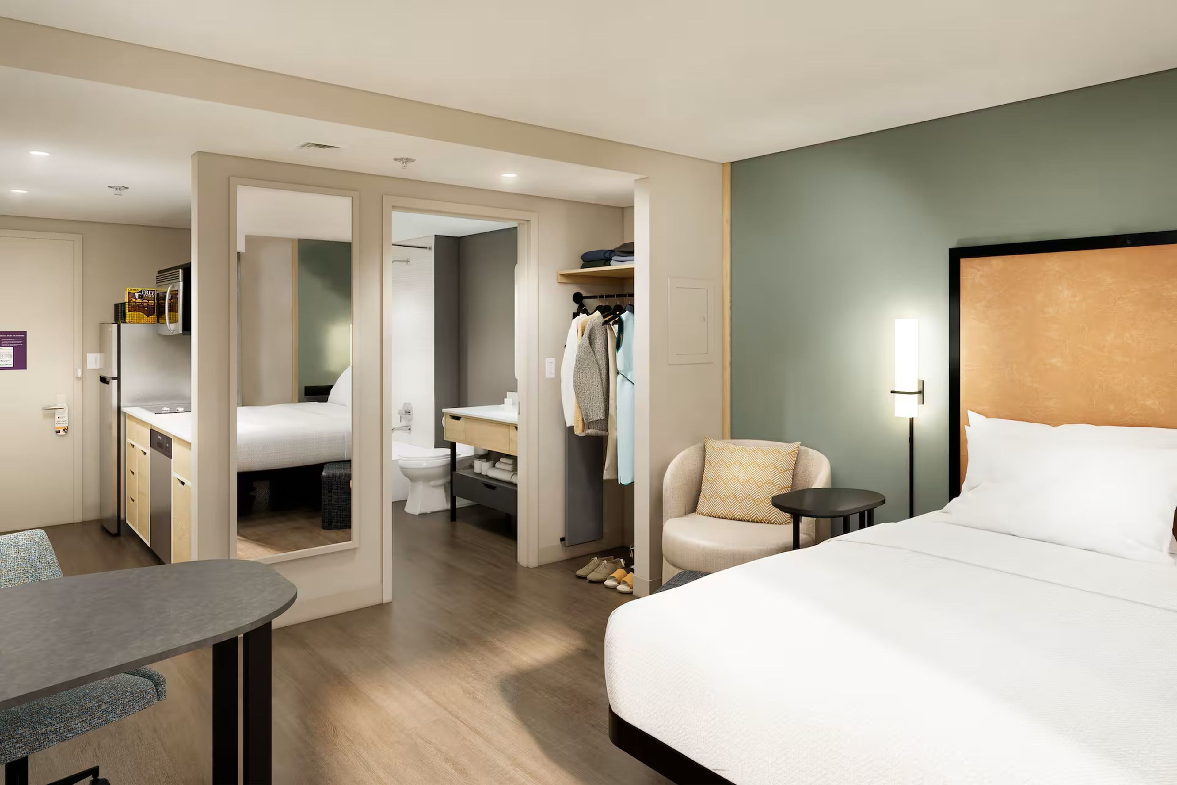 Une chambre d’hôtel comprenant un lit, un bureau, une chaise, une petite table, une armoire et une salle de bain.