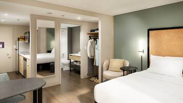 Une chambre d’hôtel comprenant un lit, un bureau, une chaise, une petite table, une armoire et une salle de bain.
