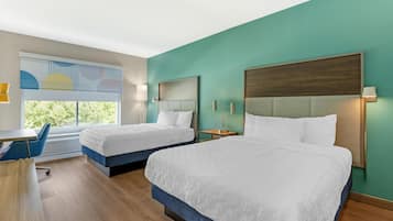 A hotel room with two beds, a desk, and a window with a view of trees.