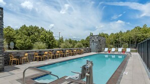 A swimming pool with a stone wall, outdoor seating, and a view of trees.
