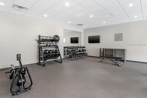 Un gimnasio con equipo de ejercicio, un televisor instalado en la pared y un tablón de anuncios con normas.