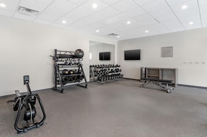 Un gimnasio con equipo de ejercicio, un televisor instalado en la pared y un tablón de anuncios con normas.