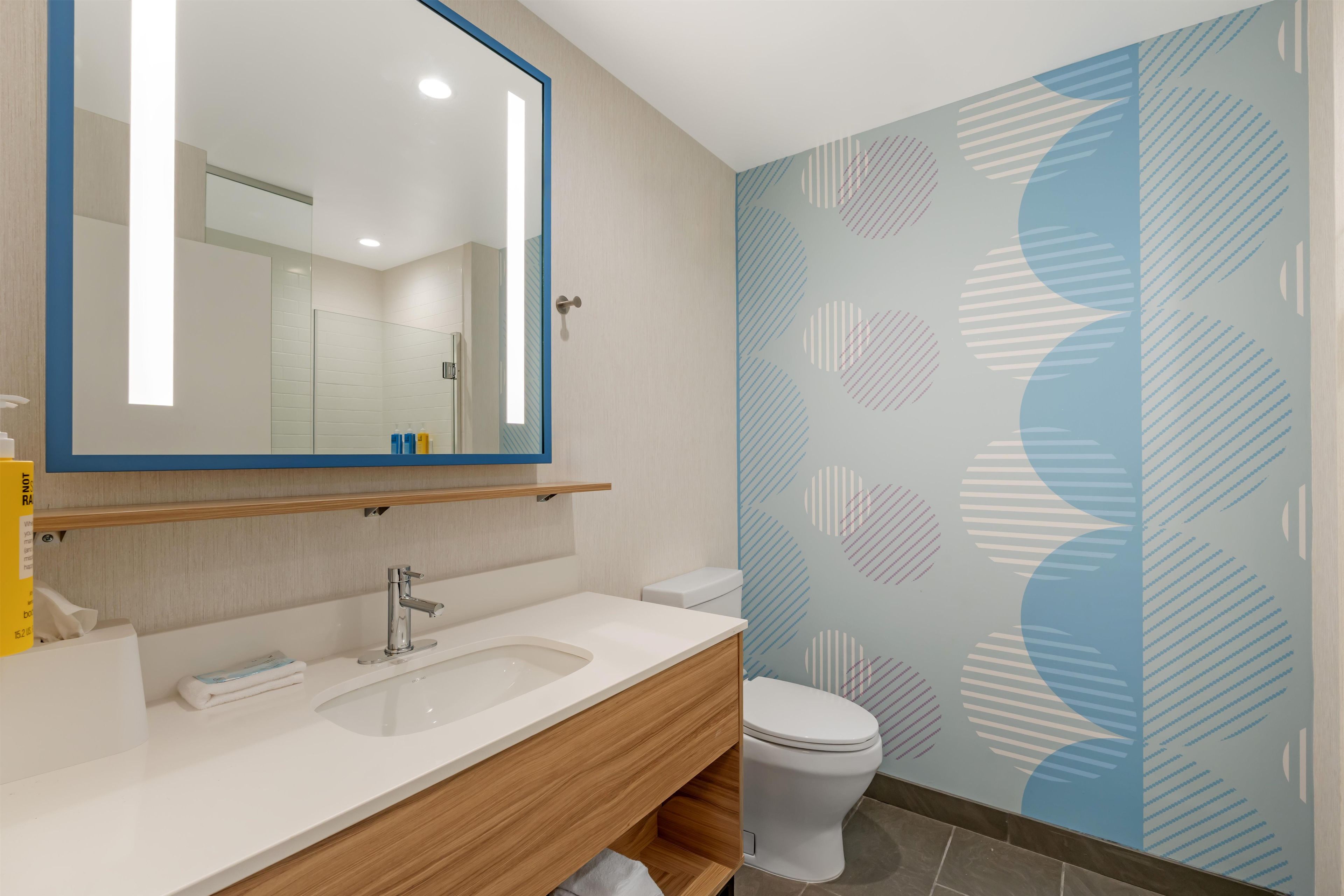 A bathroom with a white sink, a mirror, a toilet, and a patterned wall.