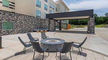 Un patio al aire libre con una mesa redonda y sillas, un muro de piedra y una zona de estar cubierta.
