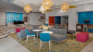 A modern hotel lobby with seating areas, a reception desk, and a TV screen.