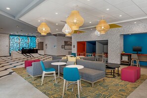A modern hotel lobby with seating areas, a reception desk, and a TV screen.